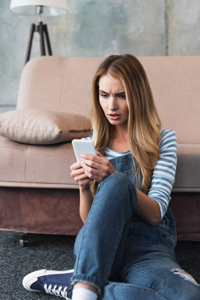 istock young upset woman using smartphone and sitting near sofa 1125698318