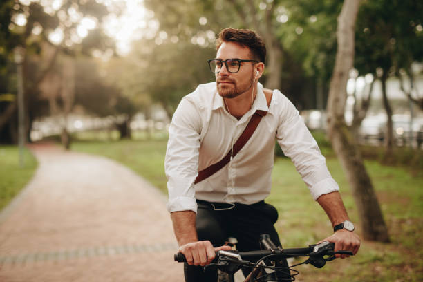 Businessman going to office on bicycle Man enjoying music using earphones while commuting to office on a bicycle. Businessman biking to office while listening to music. rush hour stock pictures, royalty-free photos & images