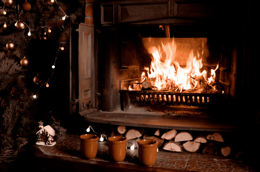 Fireplace with burning fire, three cups and Christmas tree.Warm home interior at night