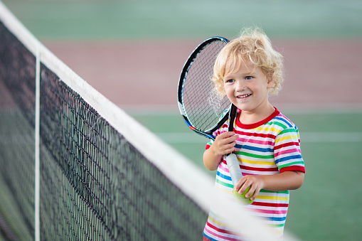 Child playing tennis on indoor court. Little boy with tennis racket and ball in sport club. Active exercise for kids. Summer activities for children. Training for young kid. Child learning to play.