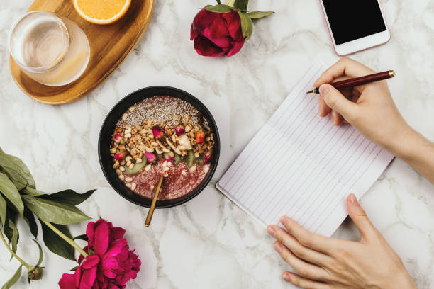 Flatlay of woman's hands with notebook and smartphone, vegan smoothie bowl with chia pudding