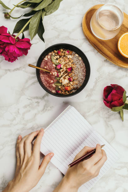 istock Flatlay of woman's hands with notebook and smartphone, vegan smoothie bowl with chia pudding topped with granola, kiwi, pine nuts and rose buds and peon flowers on marble 1125717435