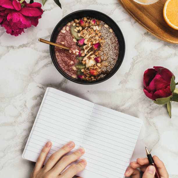 istock Flatlay of woman's hands with notebook and smartphone, vegan smoothie bowl with chia pudding topped with granola, kiwi, pine nuts and rose buds and peon flowers on marble 1125717477