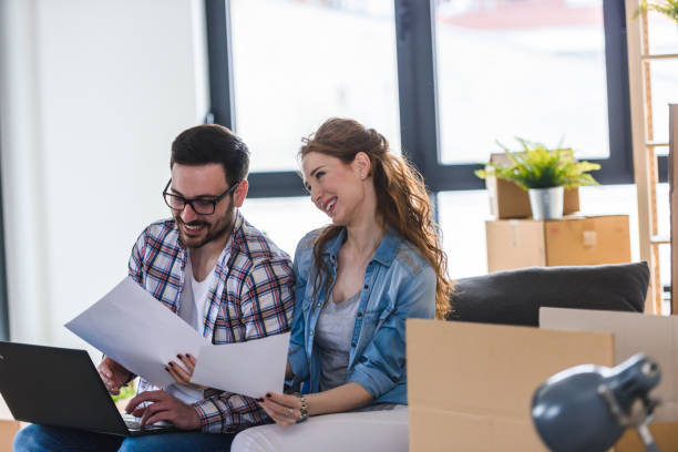 istock Happy couple sitting among unpacked cardboard boxes and using laptop computer 1125724248