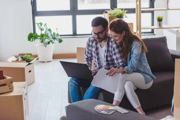 istock Happy couple sitting among unpacked cardboard boxes and using laptop computer 1125724256