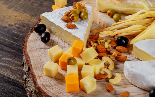 Different kinds of cheese, olives and assorted nuts wood background cheese assorted