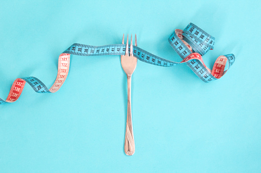 Fork, plate and measure tape on yellow background. Diet and obesity concept.