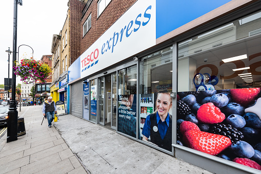London, UK - September 12, 2018: Neighborhood local store Tesco Express blue grocery shopping storefront facade exterior entrance with sign and people walking in Pimlico