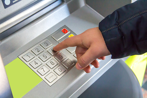 The man's hand presses the metal buttons of a silvery color on the cash machine's keyboard.