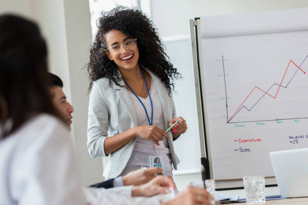 Young businesswoman gives presentation to colleagues Confident young businesswoman gives presentation to colleagues. She is standing in front of a growth chart. growth in sales stock pictures, royalty-free photos & images