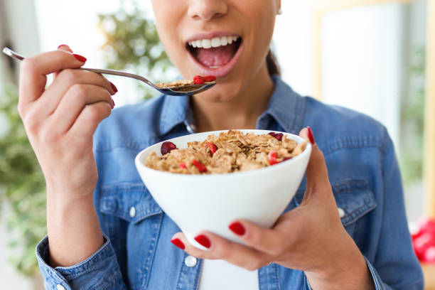 sorridente giovane donna che mangia cereali per la colazione di ciotola a casa. - eating women breakfast cereal foto e immagini stock