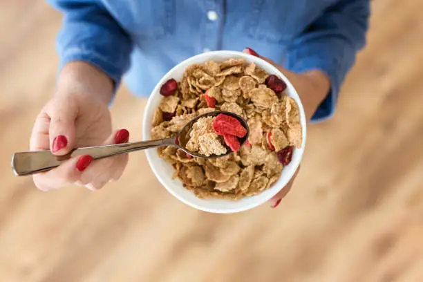 Close-up of hands of young woman holding bowl with breakfast cereals at home.