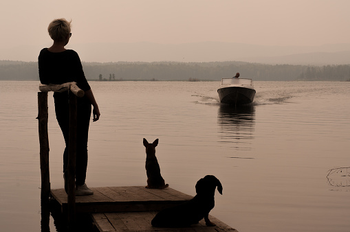 Lake Argazi, Chelyabinsk Region, Russia July 23, 2016: Girl with two dogs are standing on the pier by the lake waiting for late evening