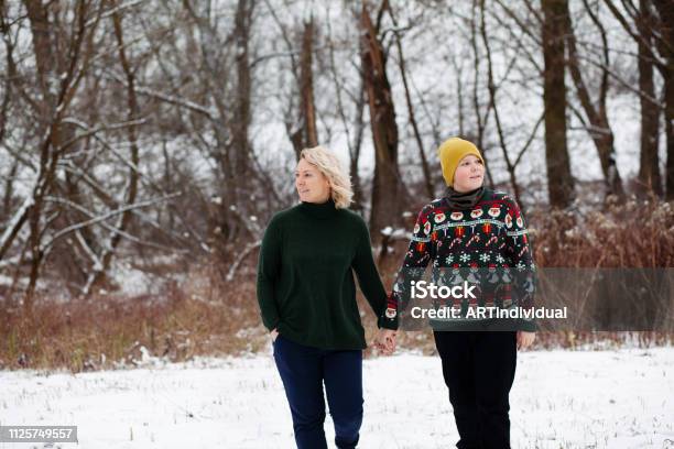 Beautiful Mother And Son Hold Hands While Walking On Snowy Ground Near To The Forest Stock Photo - Download Image Now