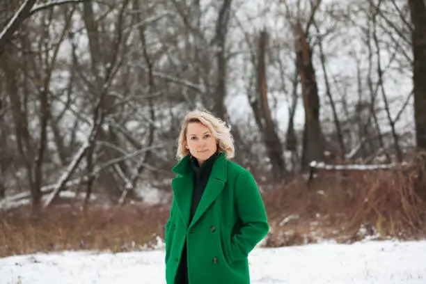 Warsaw, Poland - January 27, 2019: a pretty mature woman with curly hair pose for a camera next to a winter forest on a cold day.