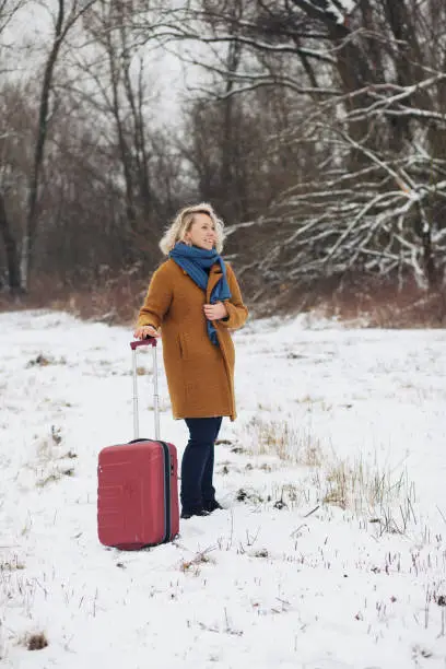 Warsaw, Poland - January 27, 2019: a pretty woman with curly hair waits for someone in snow with her suitcase.