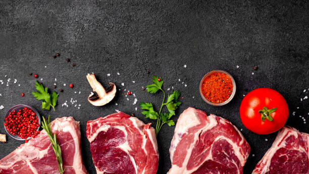 istock Meat raw steaks lie on a black background with vegetables, tomatoes, marasmade, mushrooms. background image. side view, copy space, top view 1125755285
