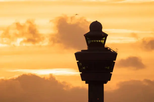 Airport control tower with a plane landing in the background during sunset.