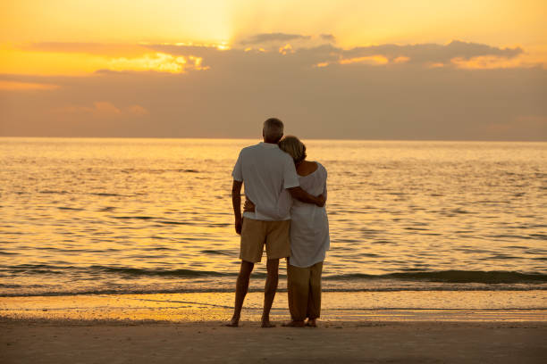 senior couple homme et femme embrassant au coucher du soleil ou au lever du soleil sur une plage tropicale déserte - shorts rear view summer beach photos et images de collection