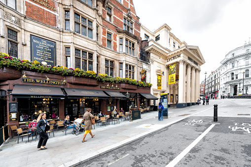 London, UK - September 12, 2018: People walking commuting on street by road with The Wellington pub restaurant sign and sidewalk in the Strand in Covent Garden