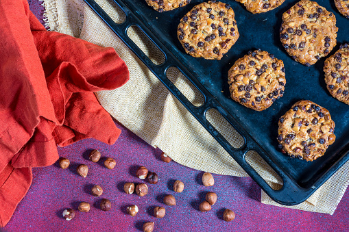 oats cookies with hazelnuts and chocolate chips on a baking sheet and some hazelnuts and cloths