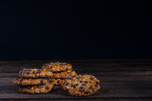 Some oats cookies with hazelnuts and chocolate chips on an old wooden table and dark background