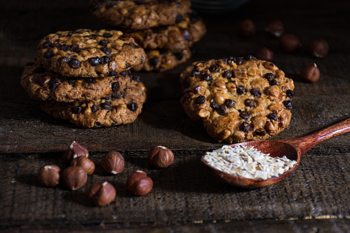 oats cookies with hazelnuts and chocolate flakes on a wood table, and a spoon with avena flakes