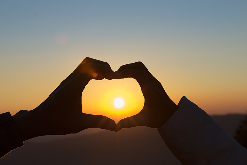 Closeup of couple making heart shape with hands and sunrise background, Happy  in love.