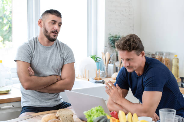 Male gay couple having an argument Mature caucasian gay male couple having an arguement while having breakfast in the morning at home sad gay stock pictures, royalty-free photos & images