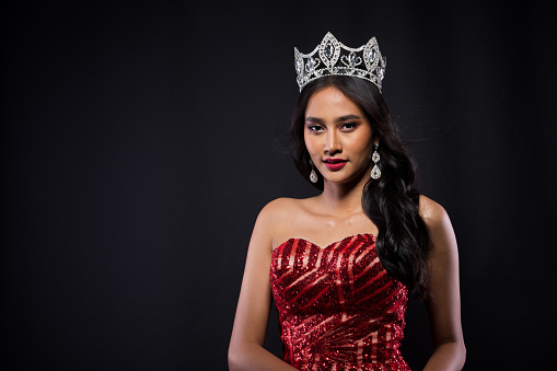 Portrait of Miss Pageant Contest in Asian woman Red Evening Ball Gown dress with Diamond Crown Sash, fashion make up face eyes love hair style, studio lighting dark background isolated copy space