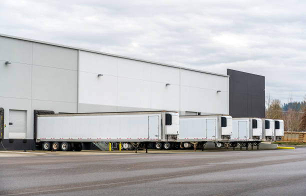 istock Long refrigerator semi trailers stand in row in warehouse docks with gates and loading cargo 1125792080