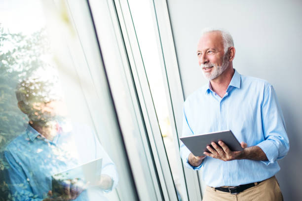 istock Senior businessman standing next to the window with tablet 1125793687