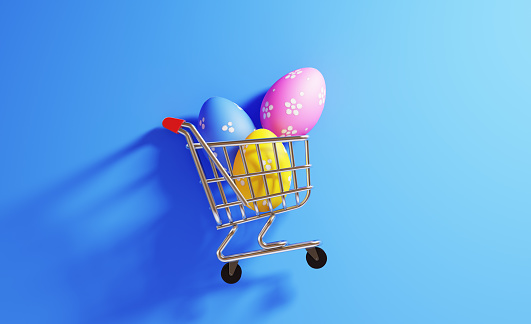 Colorful Easter eggs  in a shopping cart on blue background. Horizontal composition with  copy space. Shopping and Easter concept.