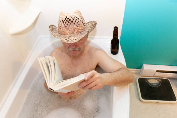 caucasian man sitting in bubble bath reading a book. - solitare imagens e fotografias de stock
