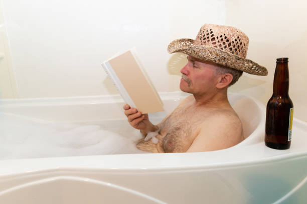 white adult male sitting in the bathtub reading a book - solitare imagens e fotografias de stock