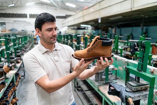 Handsome employee at a shoe factory checking a boot - Business industry concepts