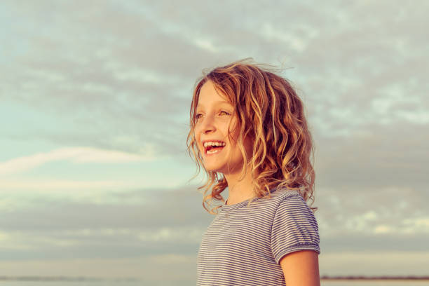 Sweet girl at dusk, golden glow at golden hour Adorable little girl with short wavy hair looks off into the distance in a cheerful, golden glowing portrait. She is a pretty 7 year old in a beautiful location, in a thoughtful and joyful moment golden hour photos stock pictures, royalty-free photos & images