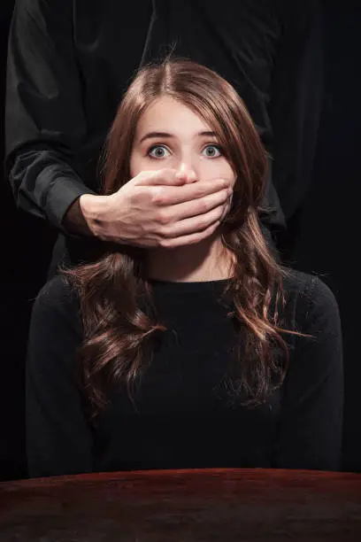 Portrait of a girl on a black background with male hands covering his mouth