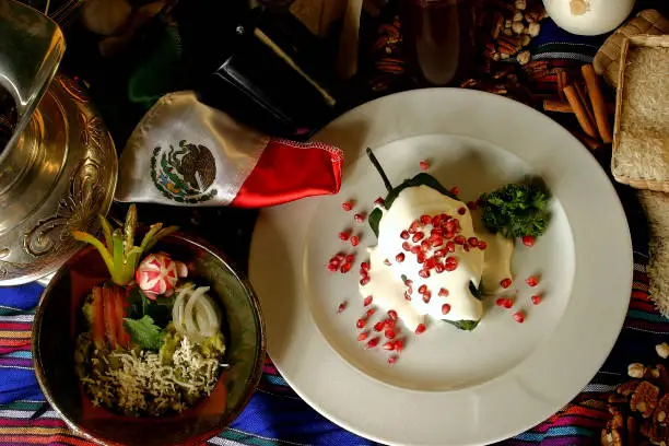 Chiles en Nogada is a dish from Mexican cuisine. It consists of poblano chilis filled with picadillo topped with a walnut-based cream sauce, called Nogada, and pomegranate seeds.