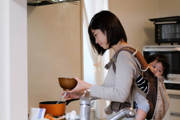 Mother cooking with baby on back at kitchen