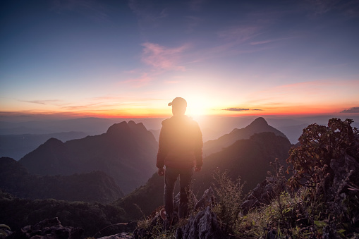 Man traveler standing on rock ridge with sunlight in wildlife sanctuary at sunset