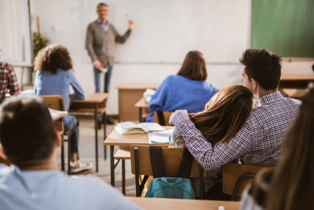 istock Back view of embraced high school couple attending a class in the classroom. 1125837727