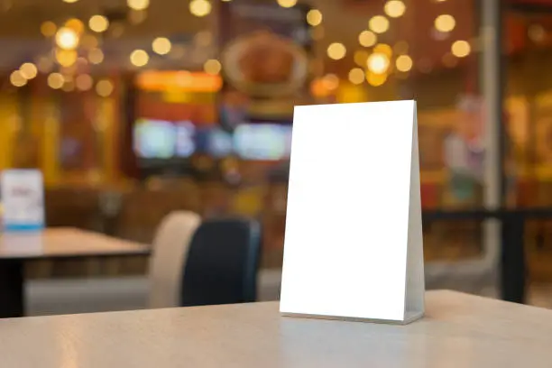 Photo of Mock up Label the blank menu frame in Bar restaurant ,Stand for booklets with white sheets paper acrylic tent card on wooden table cafeteria blurred background can inserting the text of the customer.