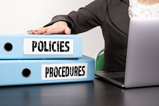 Policies and Procedures concept. Two binders on desk in the office. Business woman with laptop