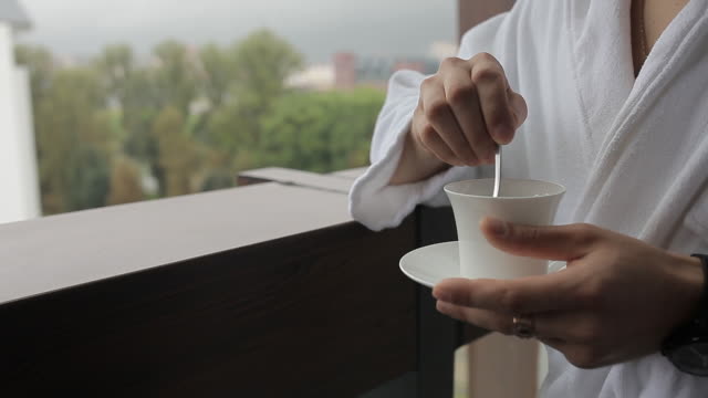 A man in a bathrobe is stirring coffee with a spoon
