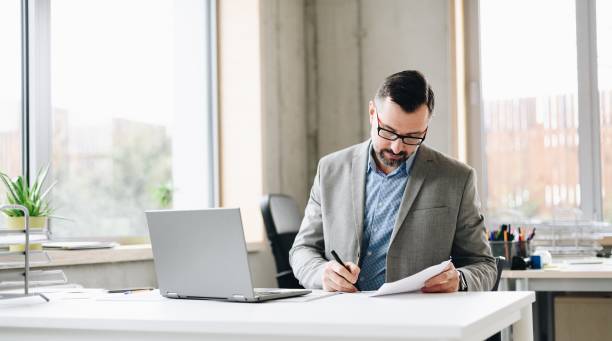 istock Middle aged handsome businessman in shirt working on laptop computer in office 1125844659