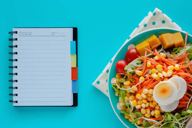 istock Fresh salad vegetable with boiled chicken egg and blank spiral notebook on blue background 1125848956