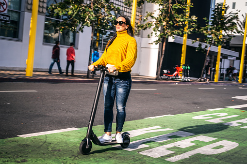 A woman in casual clothes driving an electric scooter in a scooter & bike lane downtown.