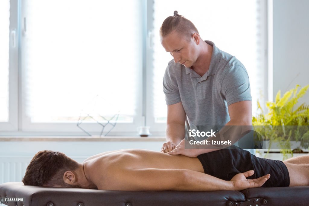 Physiotherapist massaging back of the young man Physical therapist giving back massage to young man. Patient lying down on massage table. Males Stock Photo