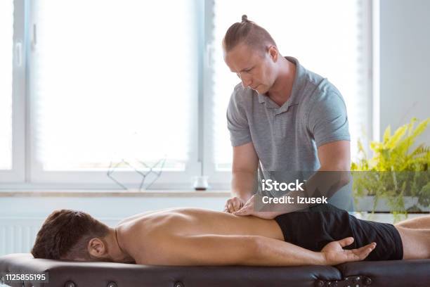 Physiotherapist Massaging Back Of The Young Man Stock Photo - Download Image Now - Males, Massage Therapist, Adult